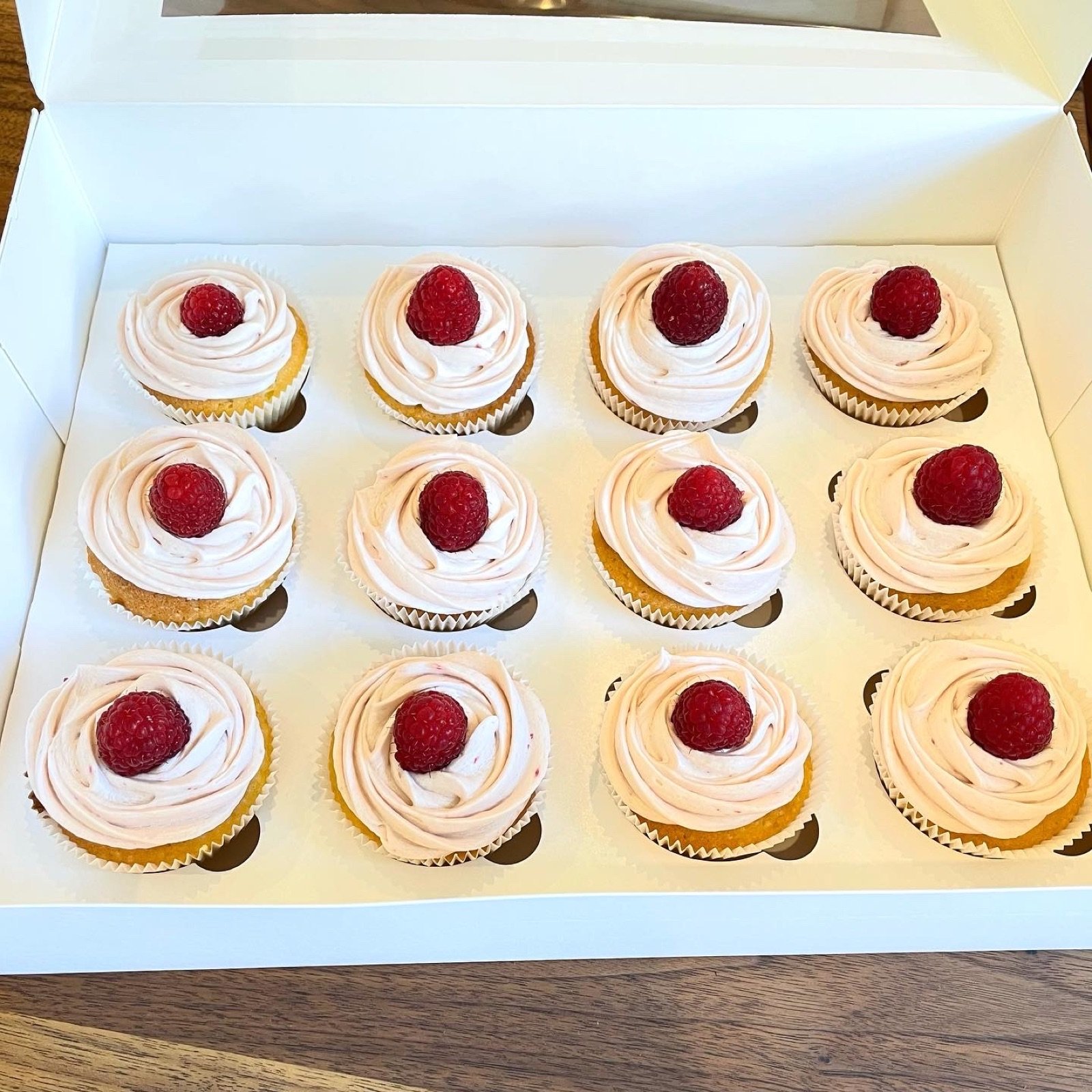 Cupcakes mit hellem Topping und Himbeeren in einer Geschenkbox